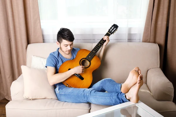 Joven con la guitarra en el sofá en la habitación — Foto de Stock