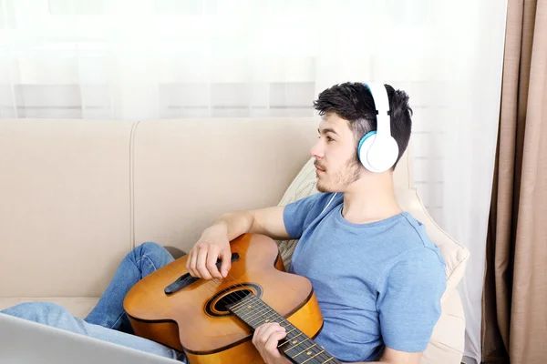Ung man med gitarr på soffa — Stockfoto