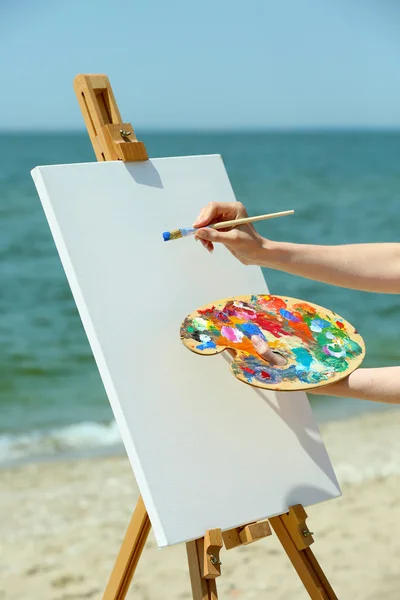 Paleta com tintas e cavalete com tela na praia — Fotografia de Stock