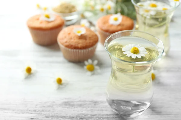 Glas Kamillentee mit Kamillenblüten und leckeren Muffins auf farbigem Holzhintergrund — Stockfoto