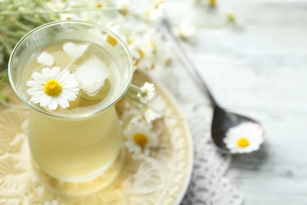 Sklo chladný Heřmánkový čaj s kostkami ledu a květy heřmánku na barevné dřevěné pozadí — Stock fotografie