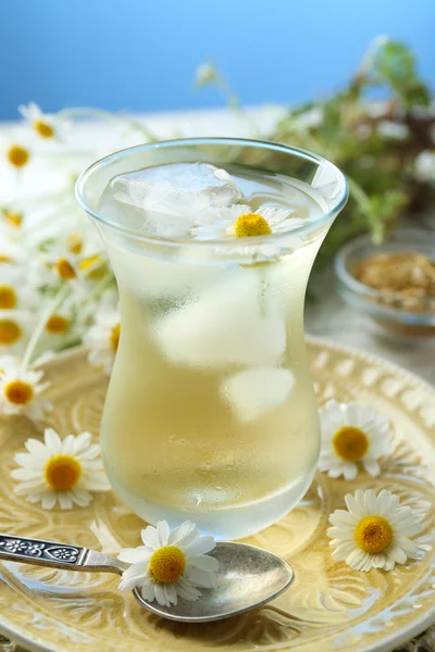 Glass of cold chamomile tea with ice cubes and chamomile flowers on table, on colorful background — Stock Photo, Image