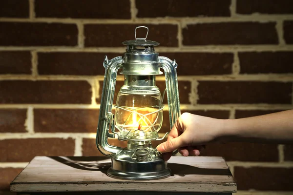 La mano enciende una lámpara de queroseno en el fondo de la pared de ladrillo — Foto de Stock
