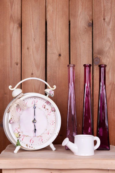 Interior design with alarm clock, decorative watering pot and vases on tabletop on wooden planks background — Stock Fotó