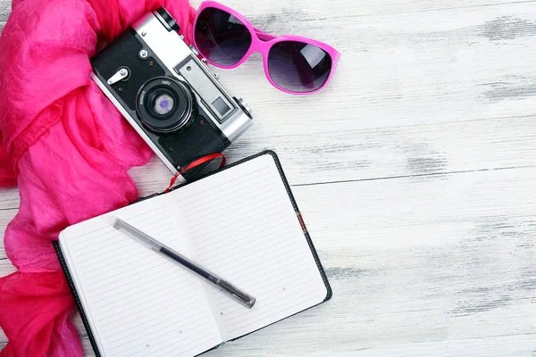 Set de turista con cuaderno abierto, cámara retro, bolígrafo y gafas de sol sobre fondo de mesa de madera —  Fotos de Stock