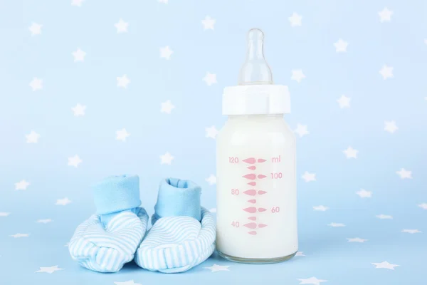 Bottiglia di latte bambino e babys bootees su sfondo blu — Foto Stock