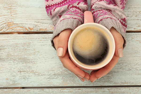 Mãos femininas segurando xícara de café no fundo de madeira — Fotografia de Stock