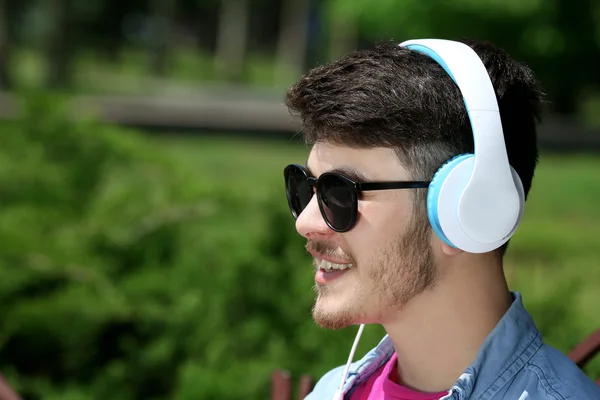 Hombre con auriculares descansando en el banco en el parque —  Fotos de Stock