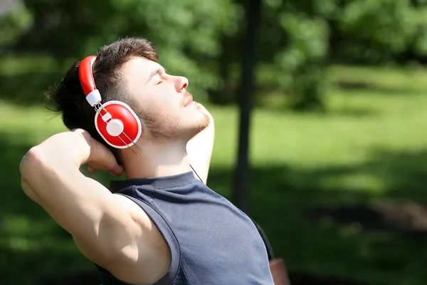 Uomo con cuffie poggiate su panchina nel parco — Foto Stock