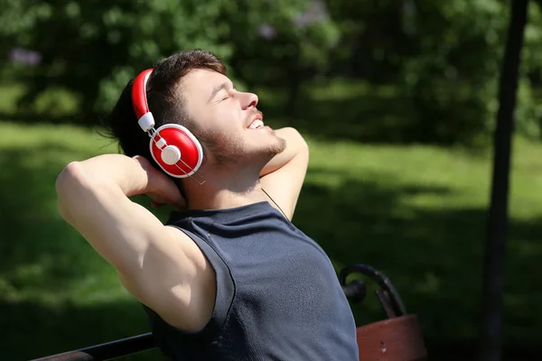 Uomo con cuffie poggiate su panchina nel parco — Foto Stock