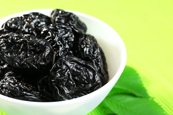 Saucer of prunes with leaves on green napkin, closeup — Stock Photo, Image