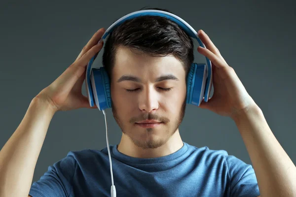 Bonito jovem ouvindo música em fundo cinza — Fotografia de Stock