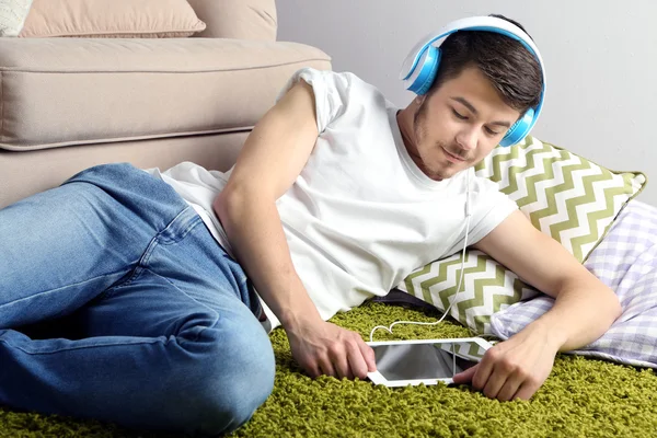 Handsome young man lying on carpet and listening to music in room — Stock Photo, Image