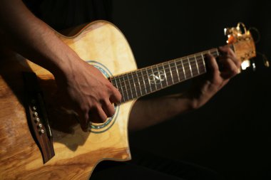 Genç adam akustik gitarla karanlık arka planda çalıyor.