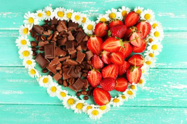 Strawberry with chocolate and chamomile in shape of heart on color wooden background
