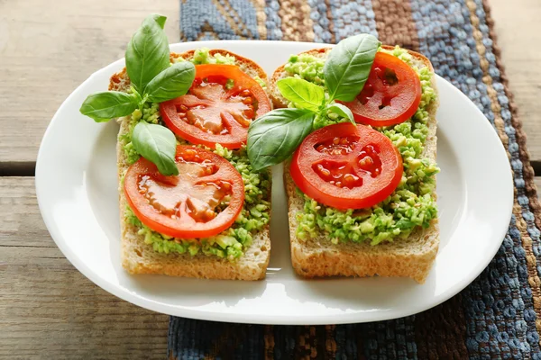 Vegansk smörgås med avokado och grönsaker på tallriken, på trä bakgrund — Stockfoto