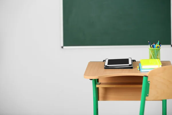 Mesa de madeira com papelaria e tablet em sala de aula sobre fundo quadro-negro — Fotografia de Stock