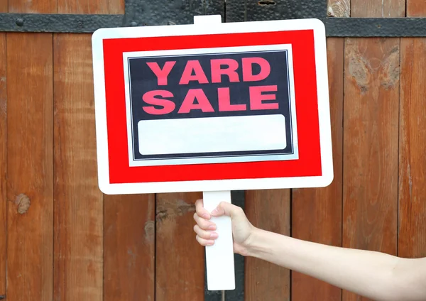 Wooden Yard Sale sign in female hand on wooden fence background — Stock Photo, Image