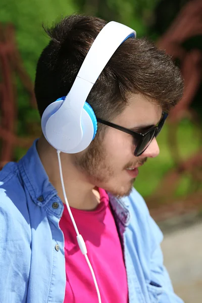 Hombre con auriculares descansando en el banco en el parque —  Fotos de Stock