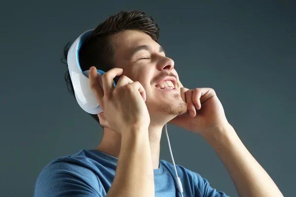 Handsome young man listening to music on grey background — Stock Photo, Image