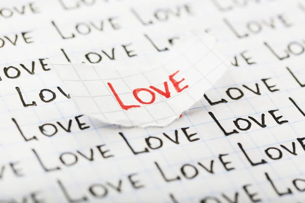 Word LOVE written on torn paper on sheet of paper background — Stock Photo, Image