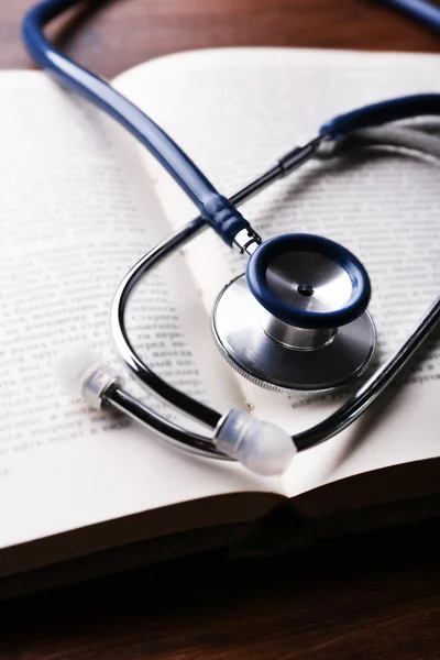 Stethoscope on book on wooden table, closeup — Stock Photo, Image