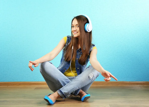 ターコイズ ブルーの壁紙の背景の上にヘッドフォンを床に座っていた若い女性 — ストック写真