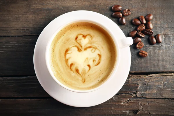 Cup of coffee latte art with grains on wooden background — Stock Photo, Image