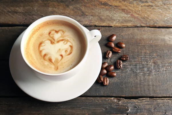 Taza de café latte arte con granos sobre fondo de madera — Foto de Stock
