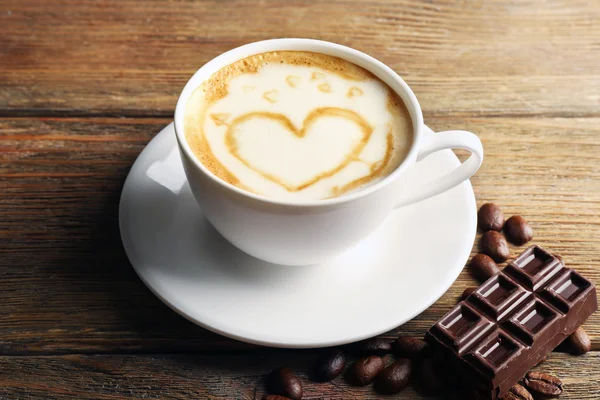 Xícara de café arte latte com grãos e chocolate sobre fundo de madeira — Fotografia de Stock