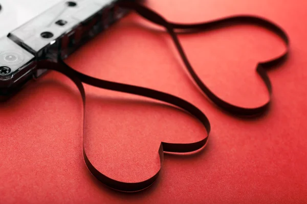 Cassette de audio con cinta magnética en forma de corazones sobre fondo rojo — Foto de Stock