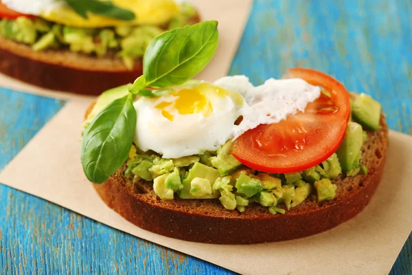 Вкусный сэндвич с яйцом, авокадо и овощами на бумажной салфетке, на фоне цвета дерева — стоковое фото
