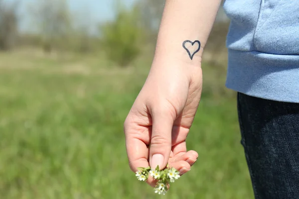 Рука молодой женщины с татуировкой на сердце, на зеленом фоне природы — стоковое фото