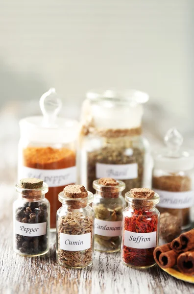 Assortiment van specerijen in glazen flessen op houten tafel, op lichte achtergrond — Stockfoto