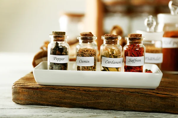 Assortiment van specerijen in glazen flessen op snijplank, op houten achtergrond — Stockfoto