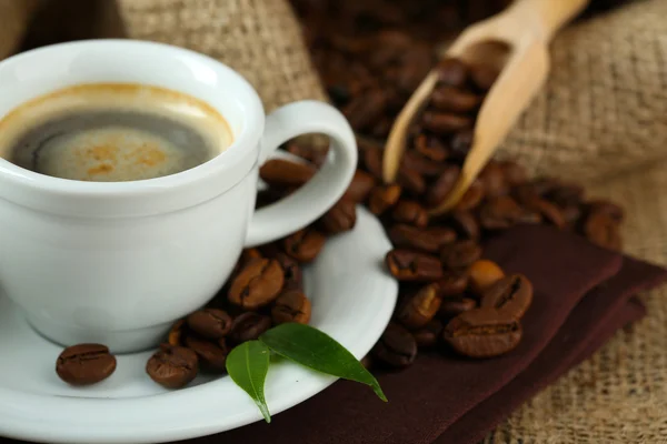Tasse Kaffee mit Bohnen auf dem Tisch aus nächster Nähe — Stockfoto