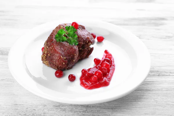 Smaczne mięso pieczone z sosem żurawinowym na talerzu, na tle drewniane kolor — Zdjęcie stockowe