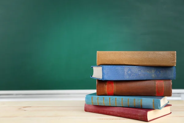 Stack of books on desk, on blackboard background — Stock Photo, Image