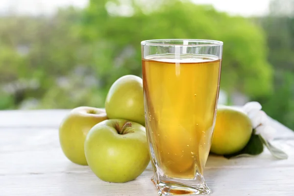 Bicchiere di succo di mela e mele sul tavolo di legno, sullo sfondo della natura — Foto Stock