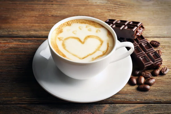 Xícara de café arte latte com grãos e chocolate sobre fundo de madeira — Fotografia de Stock