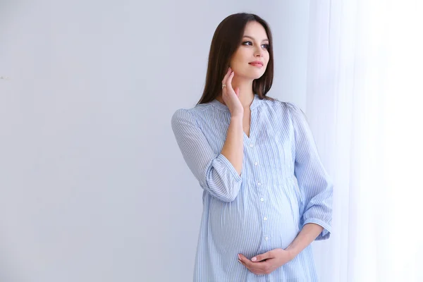 Mujer embarazada sobre fondo blanco de la pared, en interiores — Foto de Stock