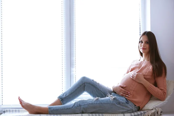 Pregnant woman sitting on windowsill background — Stock Photo, Image