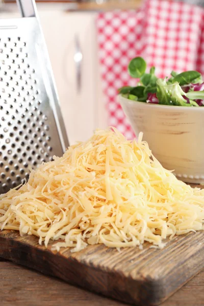 Grated cheese on wooden cutting board in kitchen — Stock Photo, Image