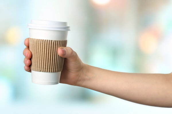 Hand holding paper cup of coffee on bright background