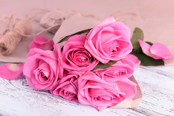 Bellissime rose rosa su tavolo in legno con pergamena, primo piano — Foto Stock