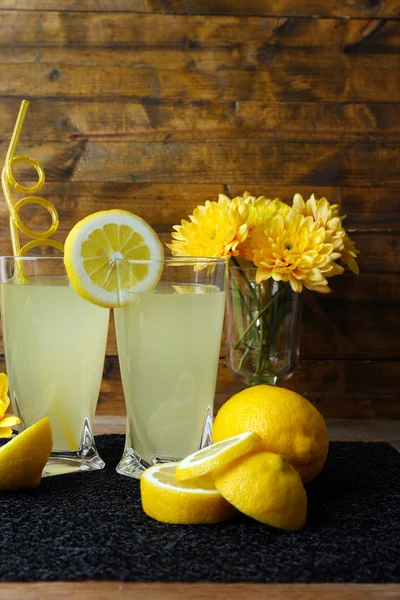 Натюрморт с лимонным соком и нарезанными лимонами на деревянном фоне — стоковое фото