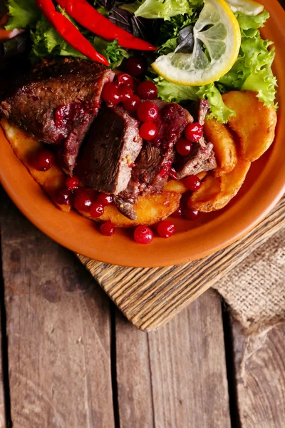 Tasty roasted meat with cranberry sauce, salad and roasted vegetables on plate, on wooden background — Stock Photo, Image