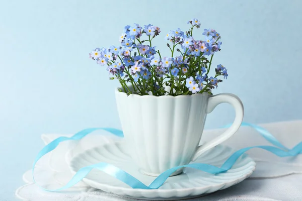 Forget-me-nots flowers in cup, on blue background — Stock Photo, Image