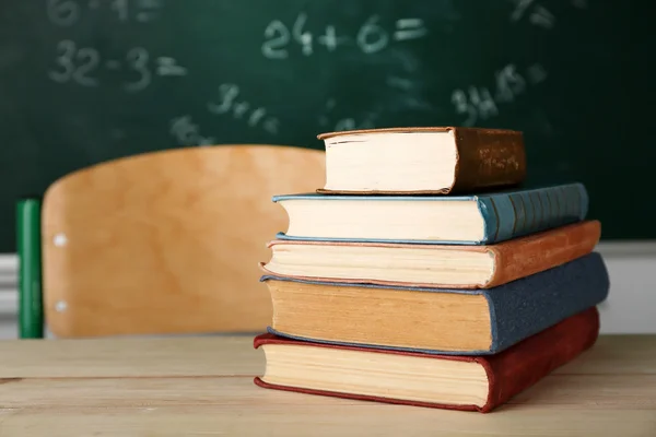 Stack of books on desk, on blackboard background — Stock Photo, Image