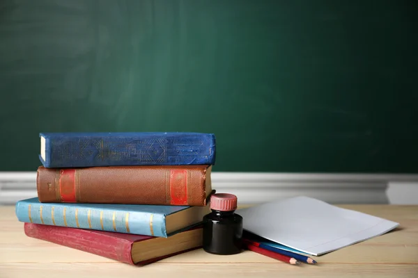 Stack of books on desk, on blackboard background — Stock Photo, Image